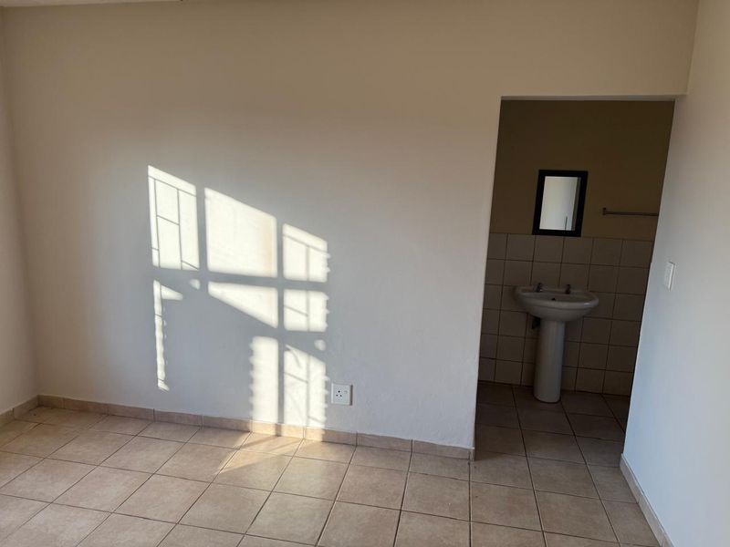 An empty bedroom featuring tiled flooring and an attached en-suite bathroom area with a pedestal basin.