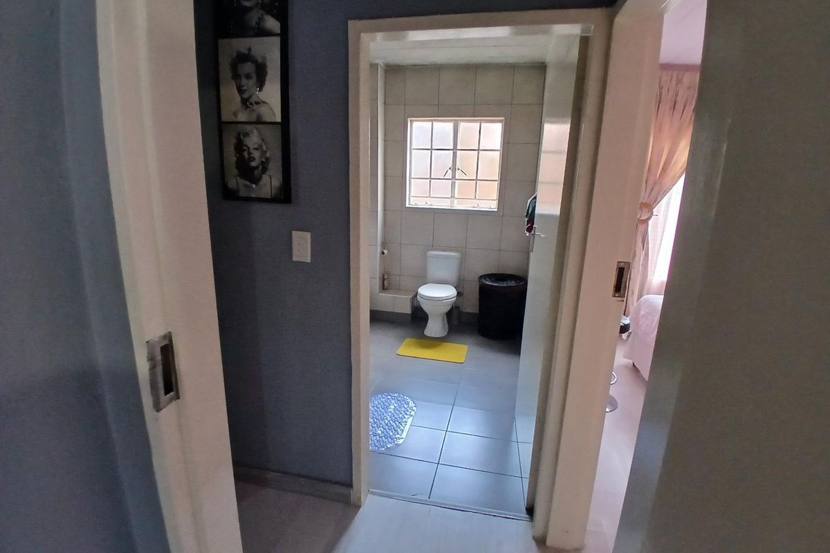 A functional bathroom featuring tiled walls and flooring, accessible from a hallway, with a standard toilet and window for natural light.