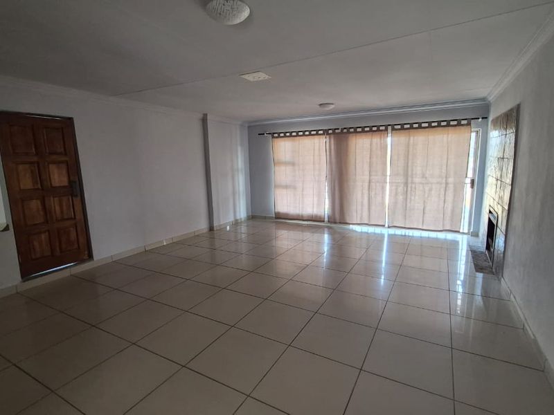 Spacious, empty living room featuring neutral tiled flooring, a built-in fireplace, and large sliding glass doors providing natural light.