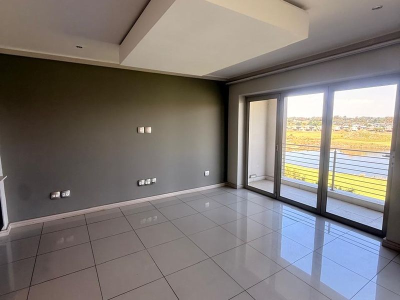 Spacious, empty living area featuring large format floor tiles, a modern recessed ceiling detail, and sliding glass doors leading to a balcony with scenic views.