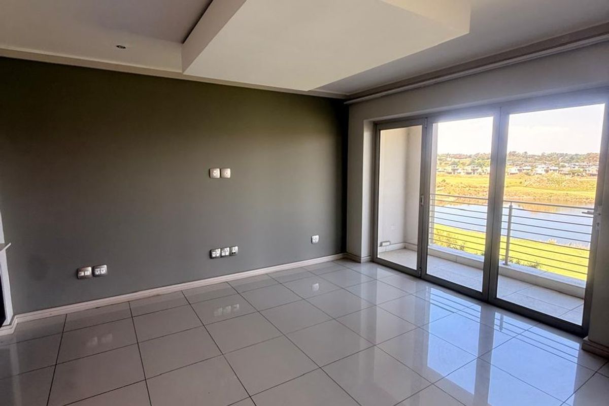 Spacious, empty living area featuring large format floor tiles, a modern recessed ceiling detail, and sliding glass doors leading to a balcony with scenic views.