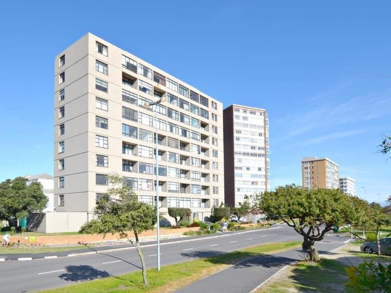 Exterior view of a multi-story apartment complex situated along a paved street with surrounding greenery and sidewalk access.