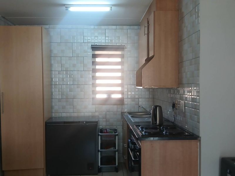 A functional kitchen featuring light wood cabinetry, tiled wall finishes, a built-in hob and oven, and a stainless steel sink.