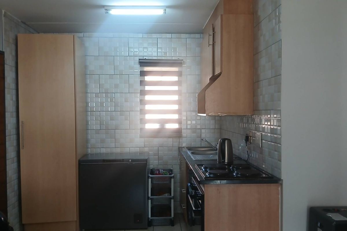 A functional kitchen featuring light wood cabinetry, tiled wall finishes, a built-in hob and oven, and a stainless steel sink.