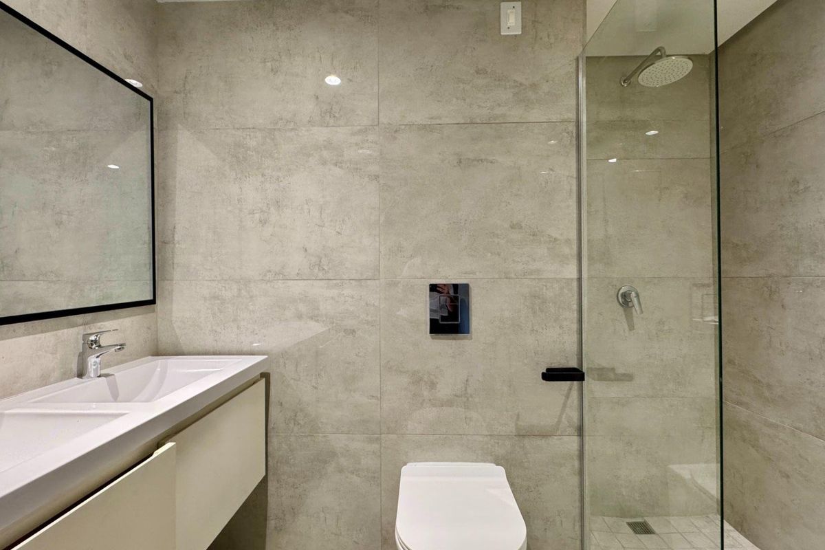 Modern bathroom featuring large format neutral wall tiles, a wall-mounted vanity, a glass-enclosed shower with a rain head, and a wall-mounted toilet.