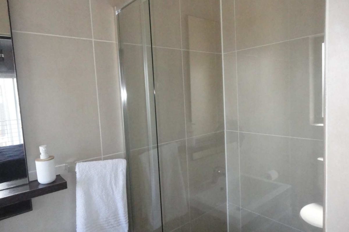 A modern bathroom featuring a glass-enclosed shower, neutral wall tiling, and a wall-mounted vanity shelf.