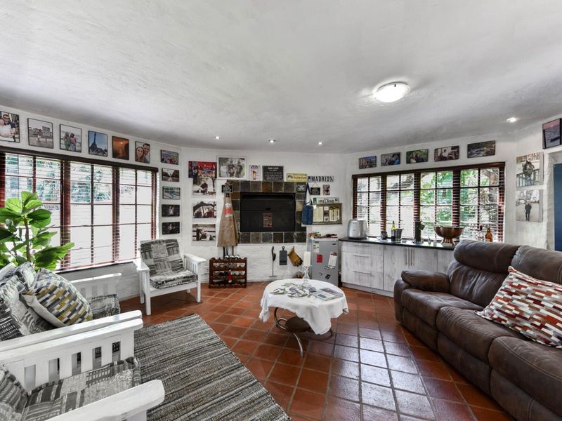 A living room featuring terracotta floor tiles, a built-in fireplace with stone surround, and built-in cabinetry under large windows.