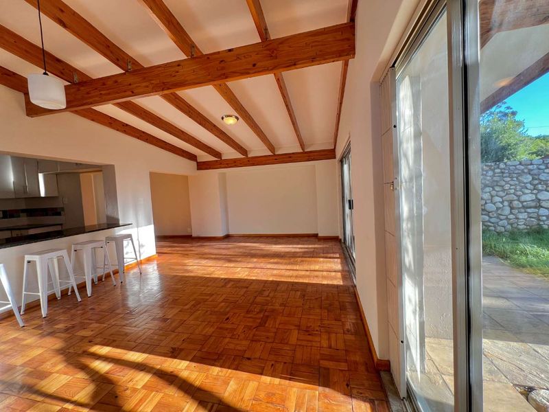 Spacious open-plan living area featuring warm parquet flooring, exposed timber ceiling beams, and large sliding glass doors that provide seamless access to the outdoors.