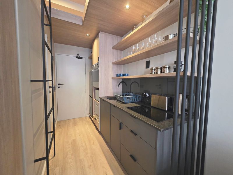 Modern compact kitchen featuring sleek dark cabinetry, stone countertops, integrated appliances, and stylish open shelving with recessed ceiling lighting.