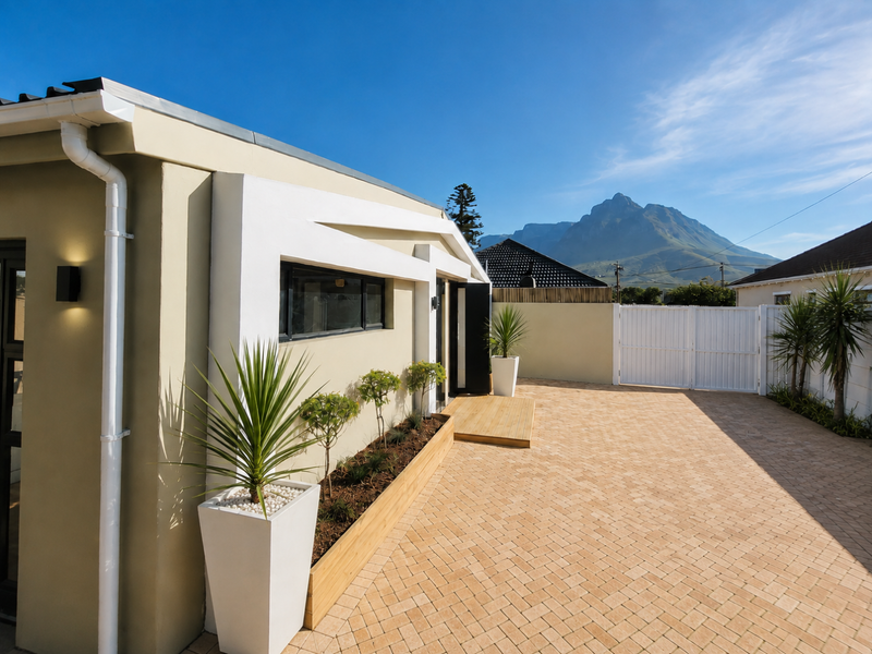 A well-maintained rear exterior area featuring paved surfacing, a timber planter box, and a small timber deck with mountain views.