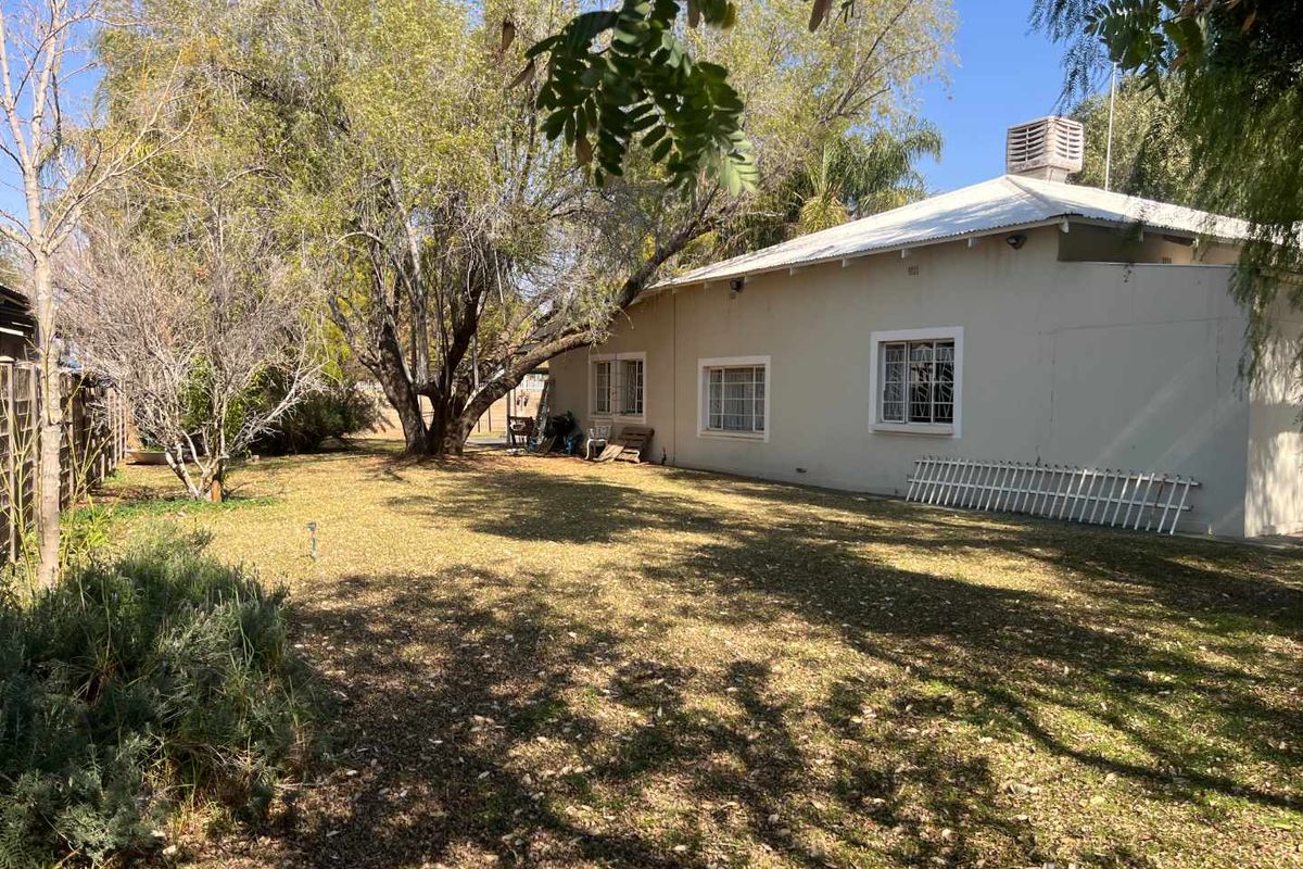 A view of the rear exterior of the house, featuring a large garden area with mature trees and a simple building facade.