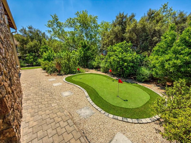A well-maintained private garden featuring a professional-style putting green, stone-paved walkway, and mature landscaping, offering a tranquil outdoor recreational space.