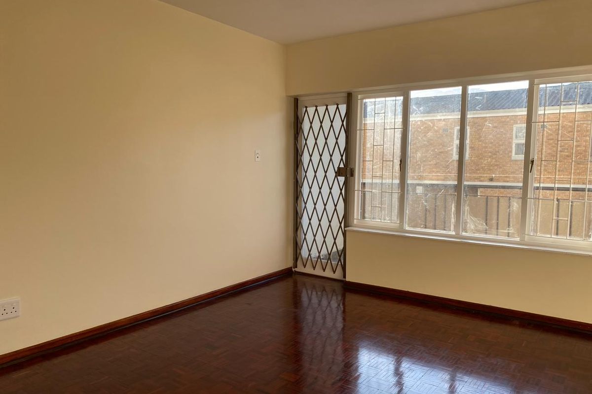 An empty living room featuring polished parquet flooring, a security gate, and large windows providing natural light.