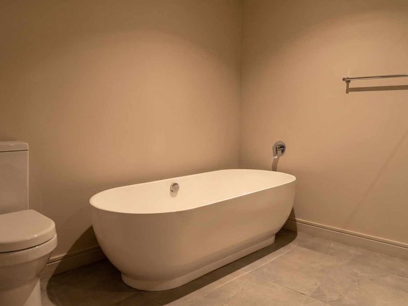 A clean and modern bathroom featuring a contemporary freestanding bathtub, a standard toilet, and neutral tiled flooring.