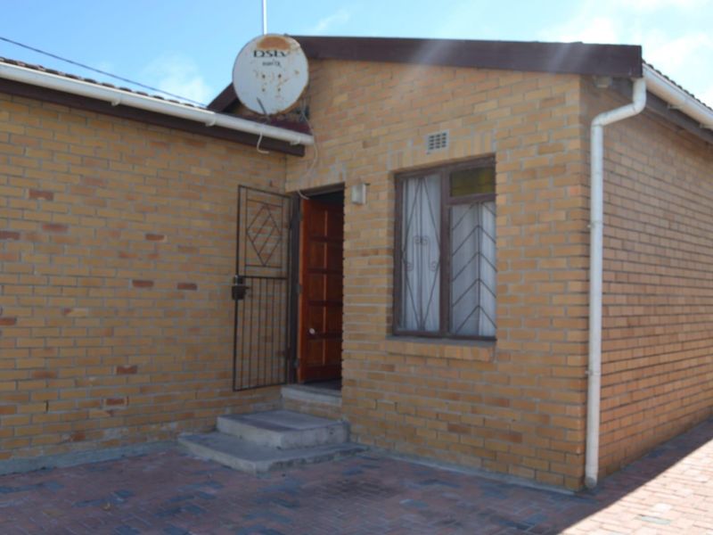 A rear exterior view of a face brick house featuring a paved courtyard, security gate, and window security bars.