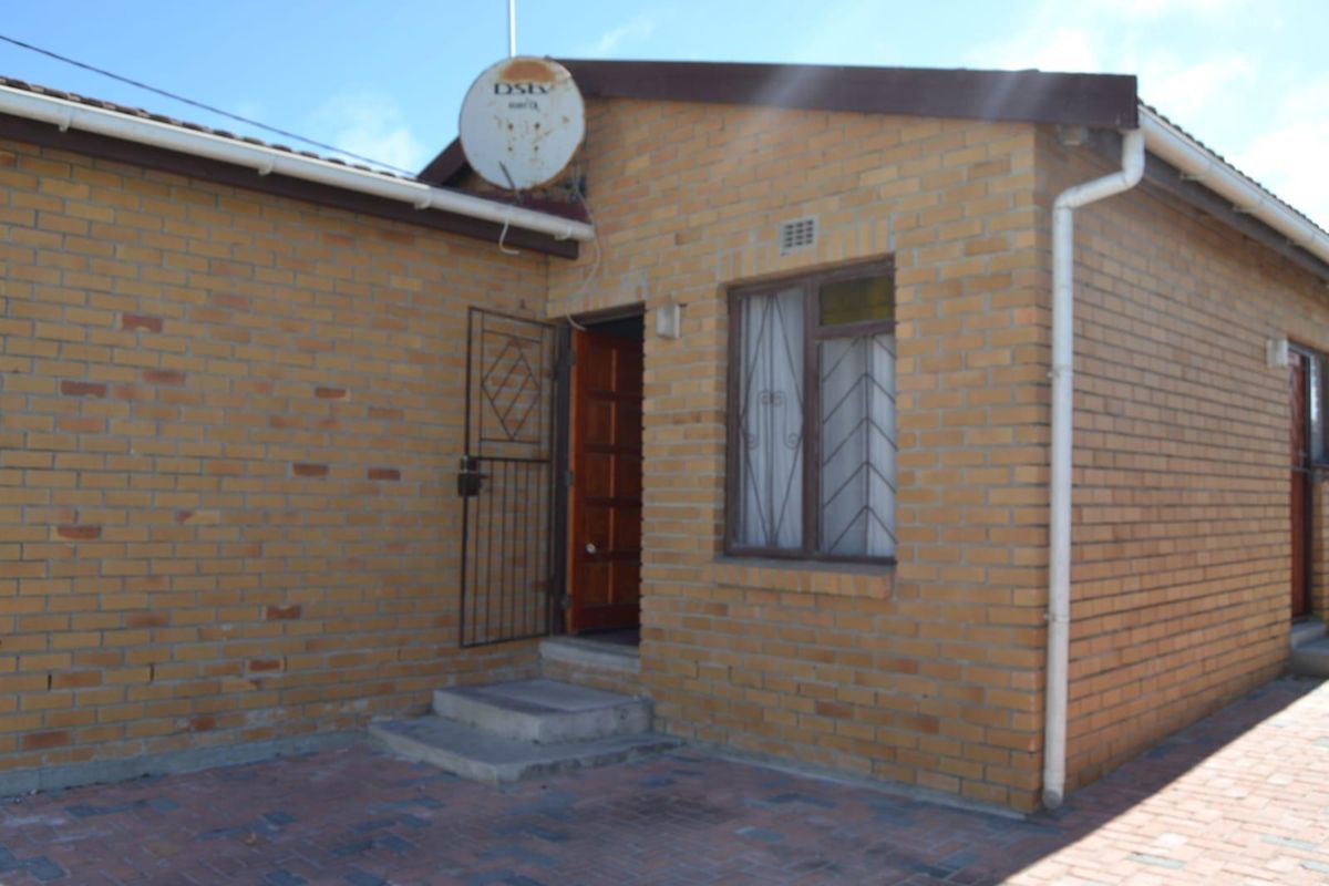 A rear exterior view of a face brick house featuring a paved courtyard, security gate, and window security bars.