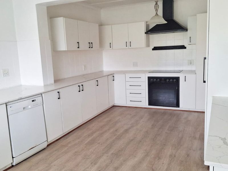 A clean, modern kitchen featuring white cabinetry, laminate countertops, built-in oven with extractor fan, and light wood-look laminate flooring.