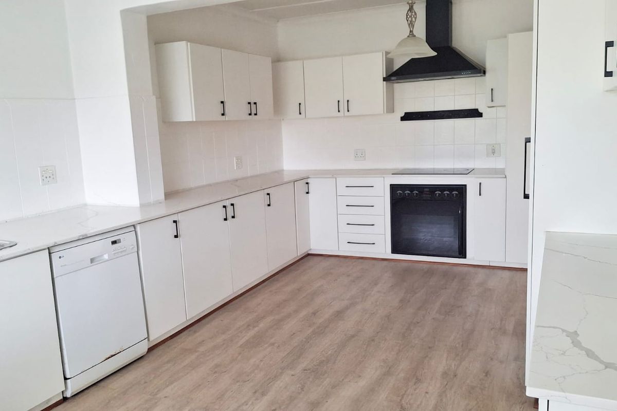A clean, modern kitchen featuring white cabinetry, laminate countertops, built-in oven with extractor fan, and light wood-look laminate flooring.