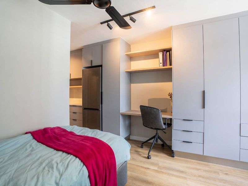 Modern bedroom featuring integrated cabinetry, a built-in desk with shelving, a ceiling fan, and light wood-look laminate flooring.