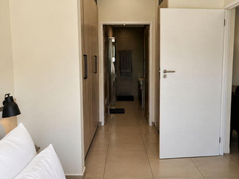 A well-maintained bedroom featuring built-in cupboards, neutral tiled flooring, and direct access to an en-suite bathroom.