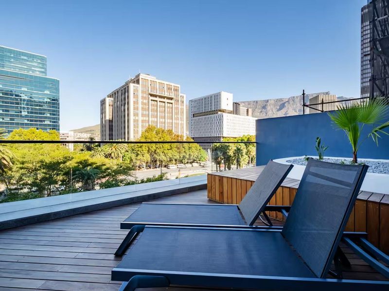 Modern balcony featuring timber decking, a glass balustrade, and a raised planter box, offering expansive city and mountain views.
