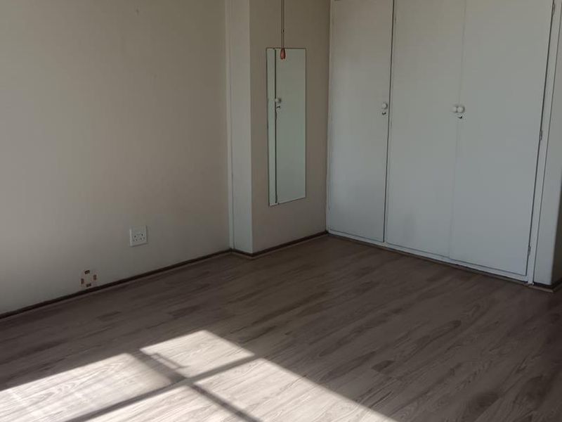 A vacant bedroom featuring light-toned laminate flooring, built-in storage cupboards, and a ceiling fan, offering a clean canvas for personalization.