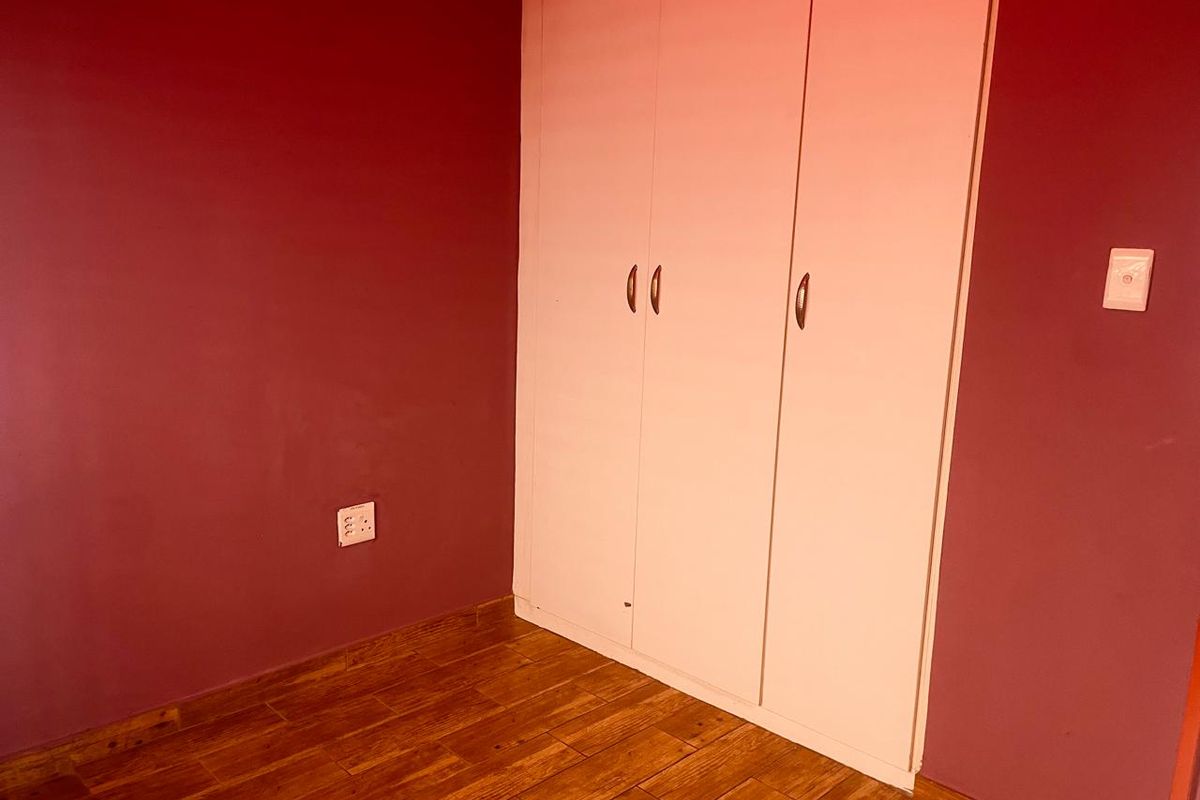 A bedroom featuring wood-look tiled flooring and a built-in white wardrobe, providing a clean and functional space.