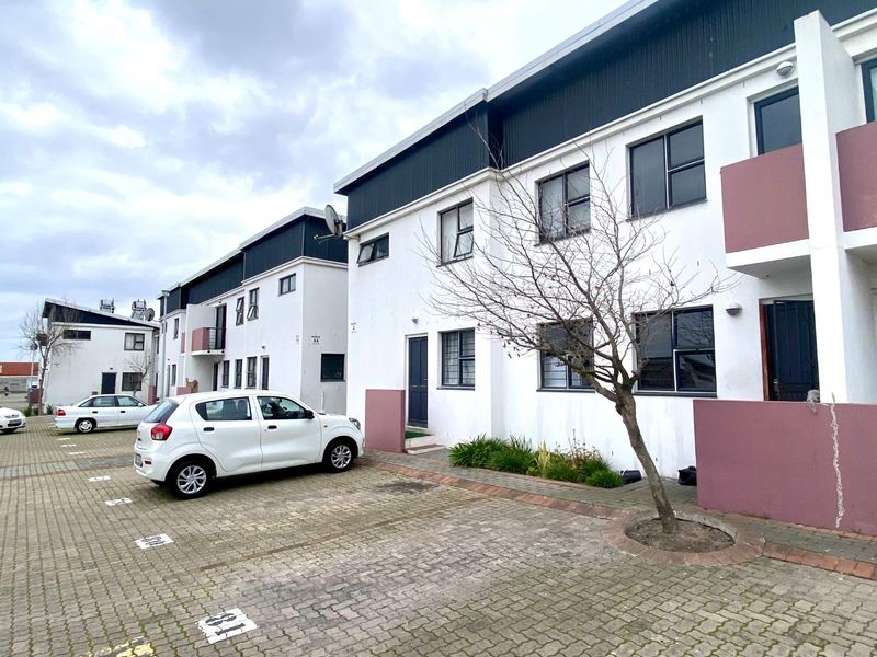 Exterior view of an apartment complex featuring paved parking bays and multi-story residential units with white and mauve facade finishes.