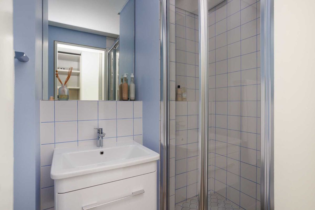 Compact bathroom featuring a white vanity with basin, a glass-enclosed shower, and blue-painted walls with tiled splashbacks.