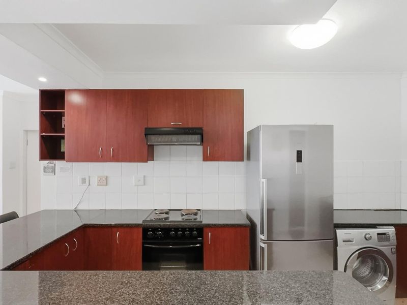 A functional kitchen featuring dark wood cabinetry, granite countertops, a tiled backsplash, and integrated cooking appliances.