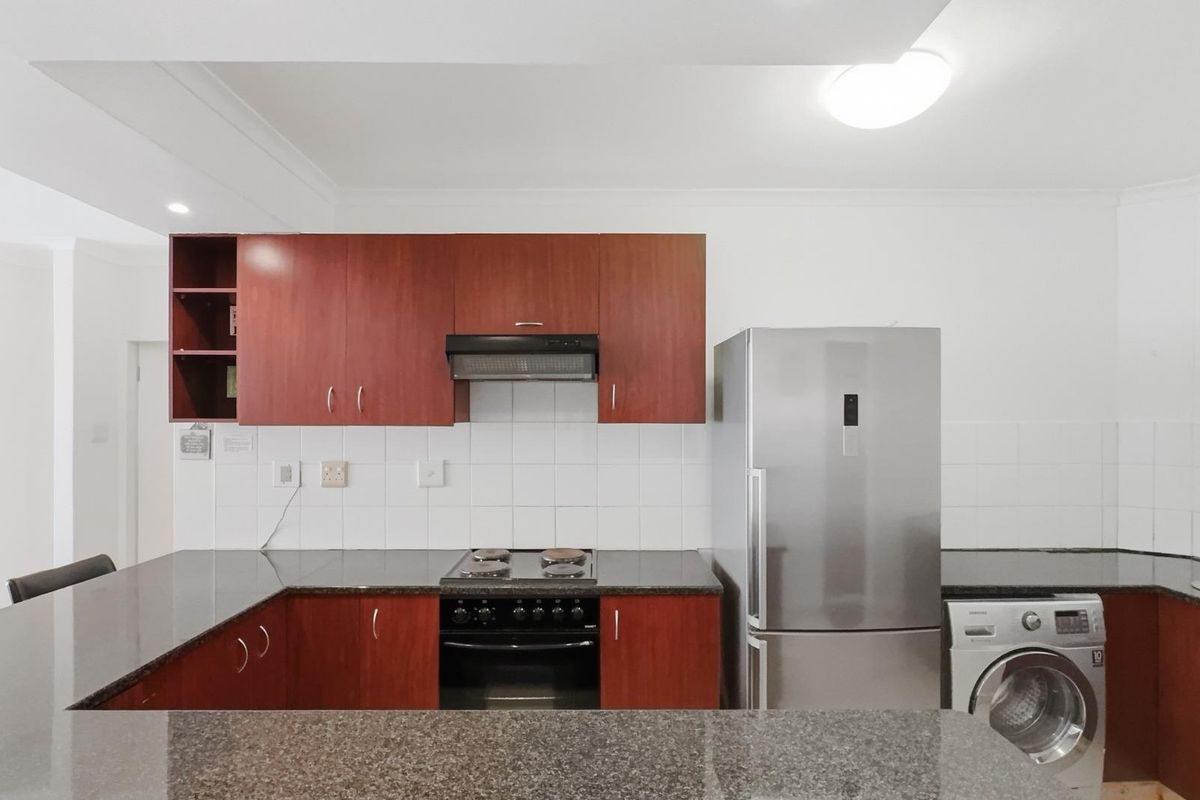 A functional kitchen featuring dark wood cabinetry, granite countertops, a tiled backsplash, and integrated cooking appliances.