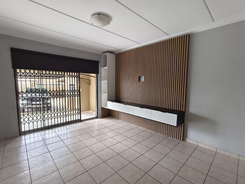 Spacious living area featuring neutral tiled flooring, a modern slatted wood feature wall, and a built-in media console with integrated shelving.