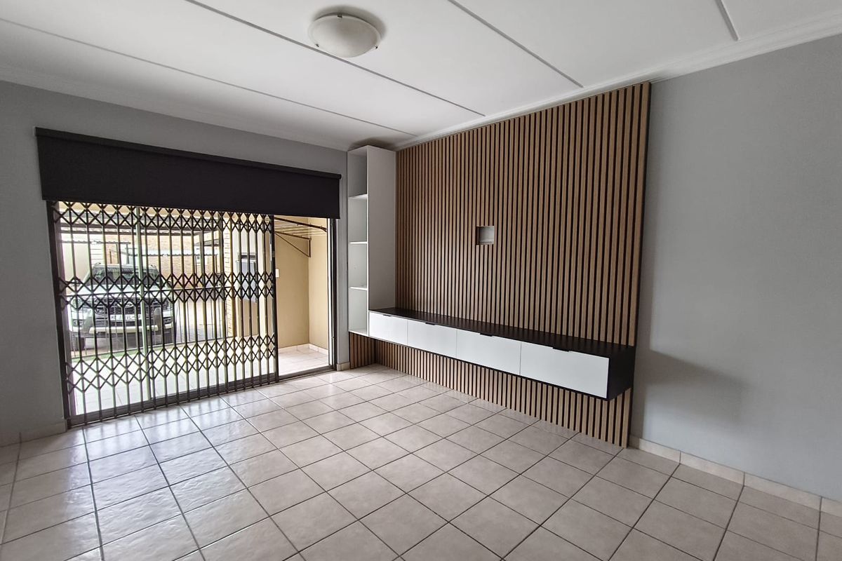 Spacious living area featuring neutral tiled flooring, a modern slatted wood feature wall, and a built-in media console with integrated shelving.