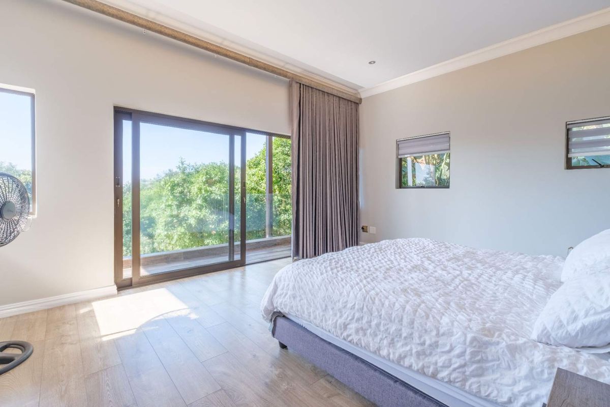 A bright and spacious bedroom featuring light wood-look flooring, large sliding glass doors leading to a balcony, and neutral wall finishes.