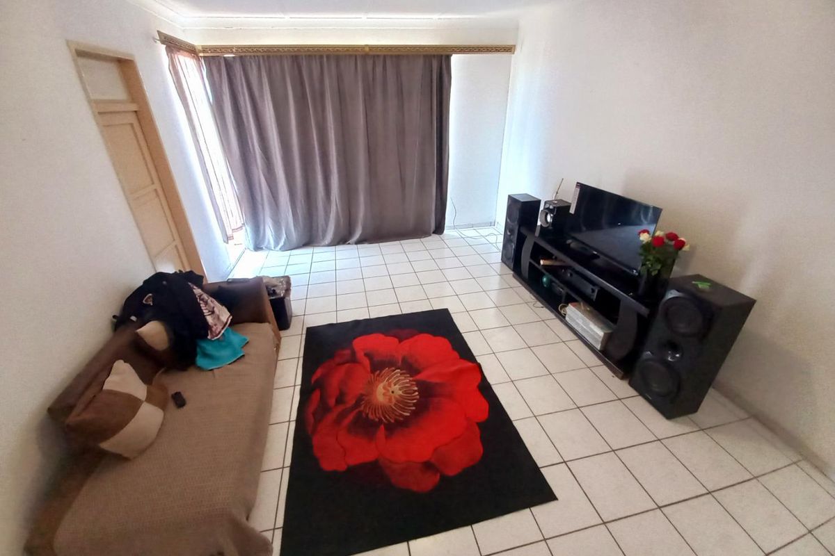 A living room featuring white tiled flooring and a large window covered by curtains, providing a functional and neutral living space.