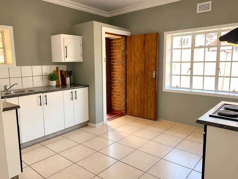 A functional kitchen featuring white cabinetry, dark laminate countertops, tiled flooring, and a built-in hob with an extractor fan.