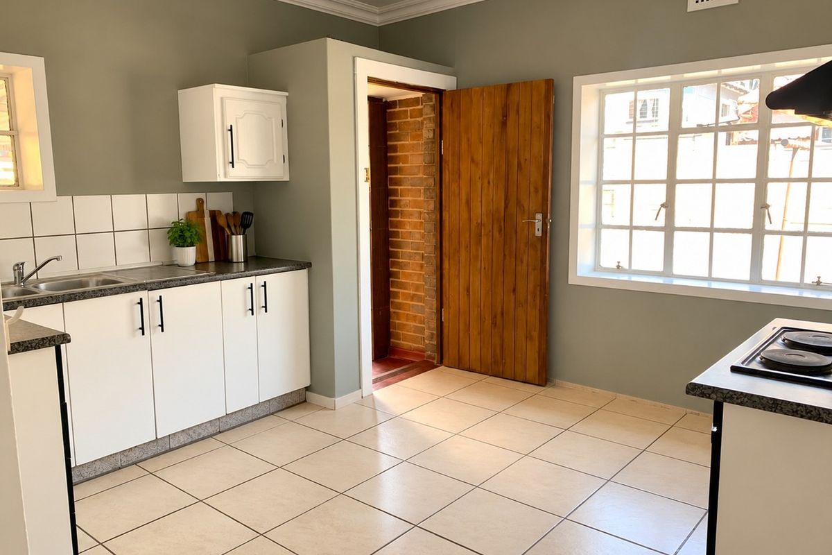 A functional kitchen featuring white cabinetry, dark laminate countertops, tiled flooring, and a built-in hob with an extractor fan.
