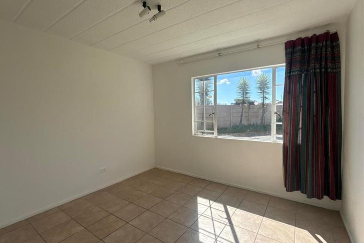 A bright, empty bedroom featuring tiled flooring, a large window with natural light, and a simple ceiling-mounted light fixture.