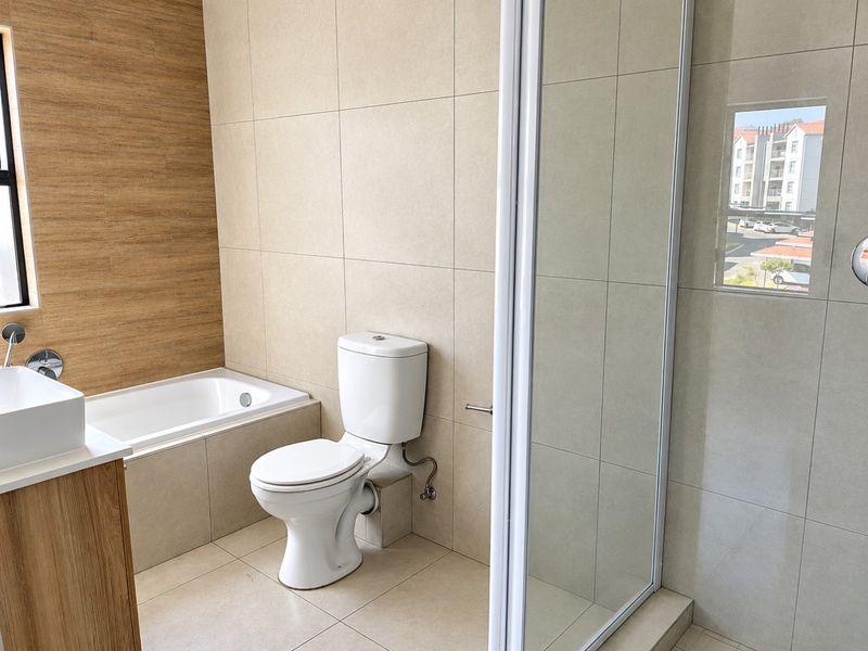 Modern bathroom featuring a built-in bathtub, separate shower enclosure, toilet, and a vanity cabinet with a basin, finished with neutral wall and floor tiles.