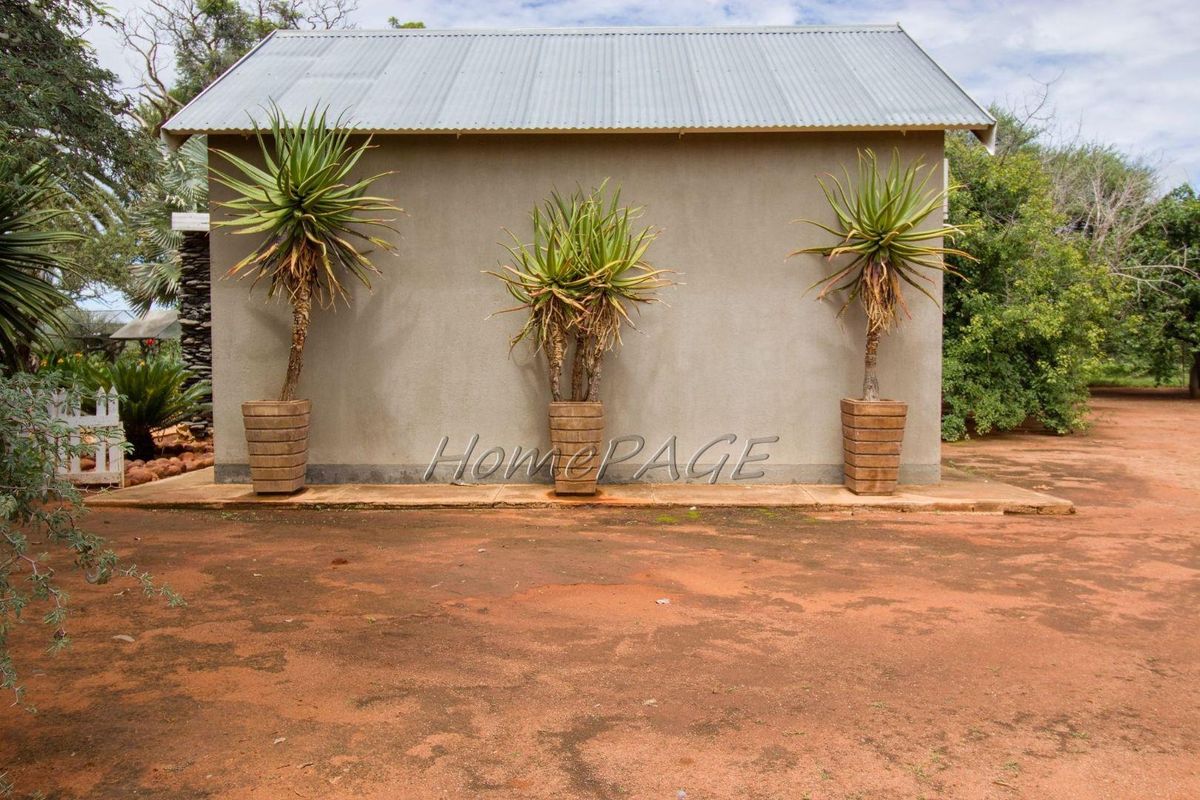 A side view of a small holding outbuilding featuring a corrugated metal roof and a concrete apron set against a natural landscape.