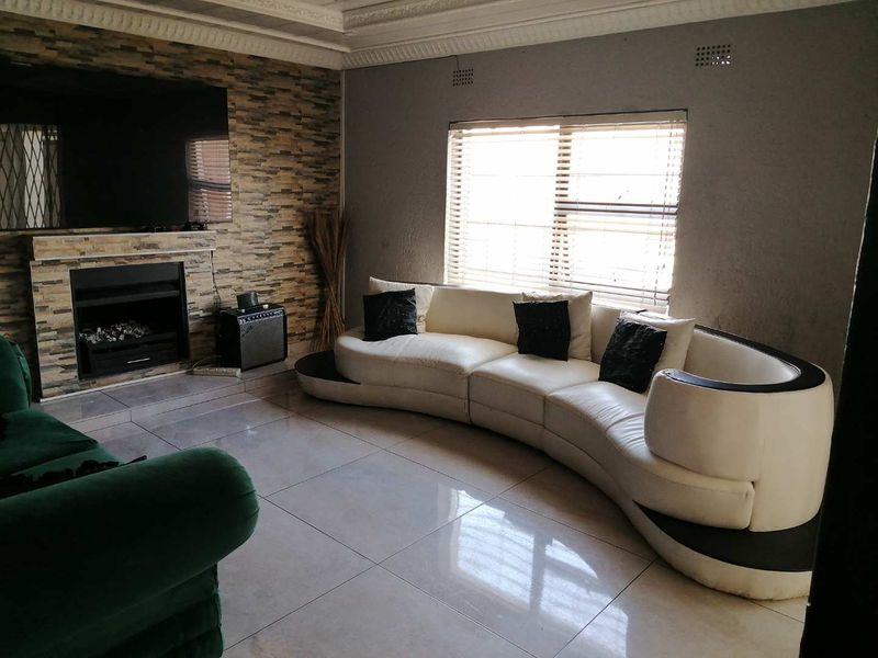 Living room featuring a stone-clad fireplace, large format floor tiles, and decorative ceiling cornicing, providing a functional space with potential for cosmetic updates.