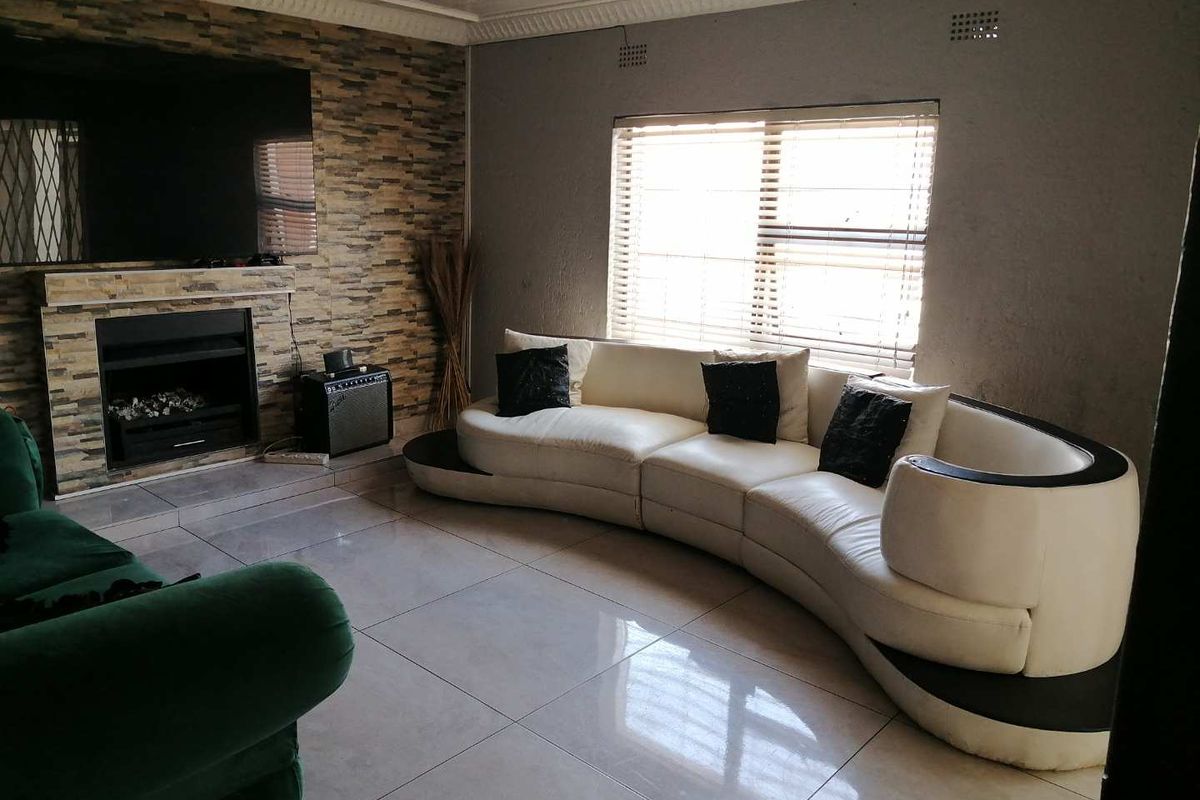 Living room featuring a stone-clad fireplace, large format floor tiles, and decorative ceiling cornicing, providing a functional space with potential for cosmetic updates.