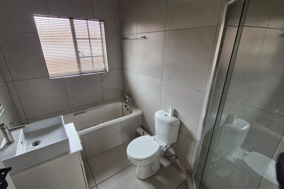 A modern bathroom featuring a built-in bathtub, separate shower enclosure, toilet, and a vanity basin with neutral wall and floor tiling.