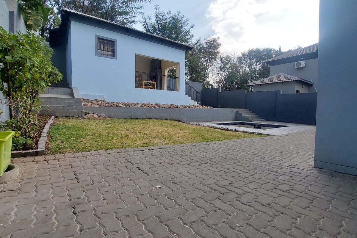 Rear exterior view featuring a paved courtyard, a small swimming pool, a lawn area, and a covered patio attached to the main dwelling.