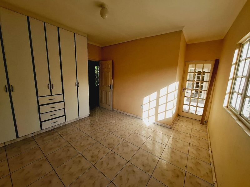 A vacant bedroom featuring built-in cupboards, tiled flooring, and a glass-paneled french door allowing natural light.