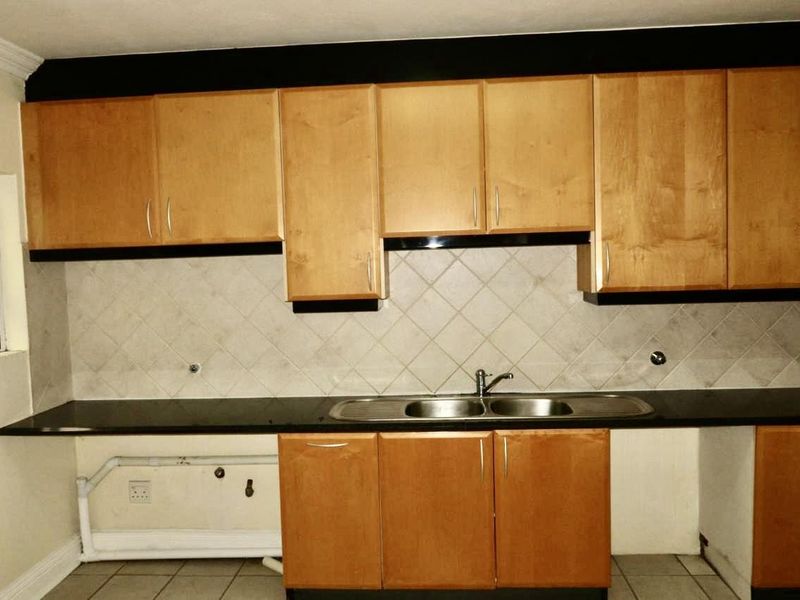 A dated kitchen featuring wooden cabinetry, a double basin sink, and a tiled backsplash, currently requiring minor repairs and cosmetic updates.