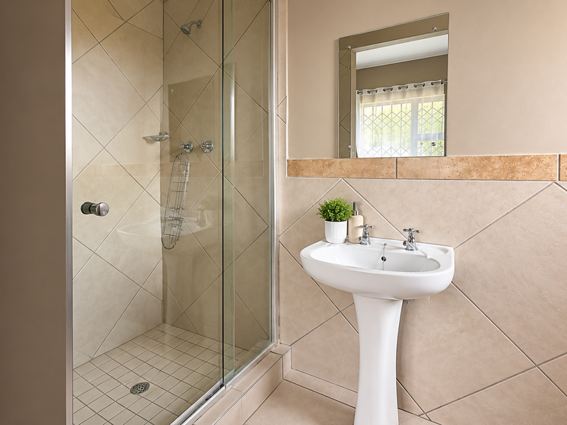 A clean bathroom featuring a pedestal basin, a glass-enclosed shower, and neutral-toned wall and floor tiling.