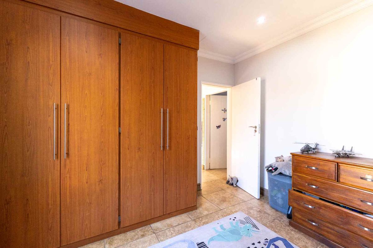 A bedroom featuring extensive built-in wooden cupboards, tiled flooring, and recessed lighting, providing ample storage and a neutral foundation.