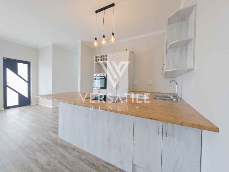 Modern open-plan kitchen featuring light wood-grain cabinetry, laminate countertops, built-in oven, and sleek pendant lighting, seamlessly integrated with the living area.