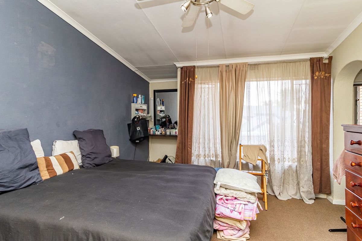 A bedroom featuring a ceiling fan, built-in shelving, and an arched doorway, with carpeted flooring and a large window with curtains.